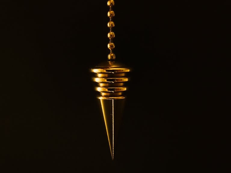 An elegant gold pendulum with chain on a mysterious black background.