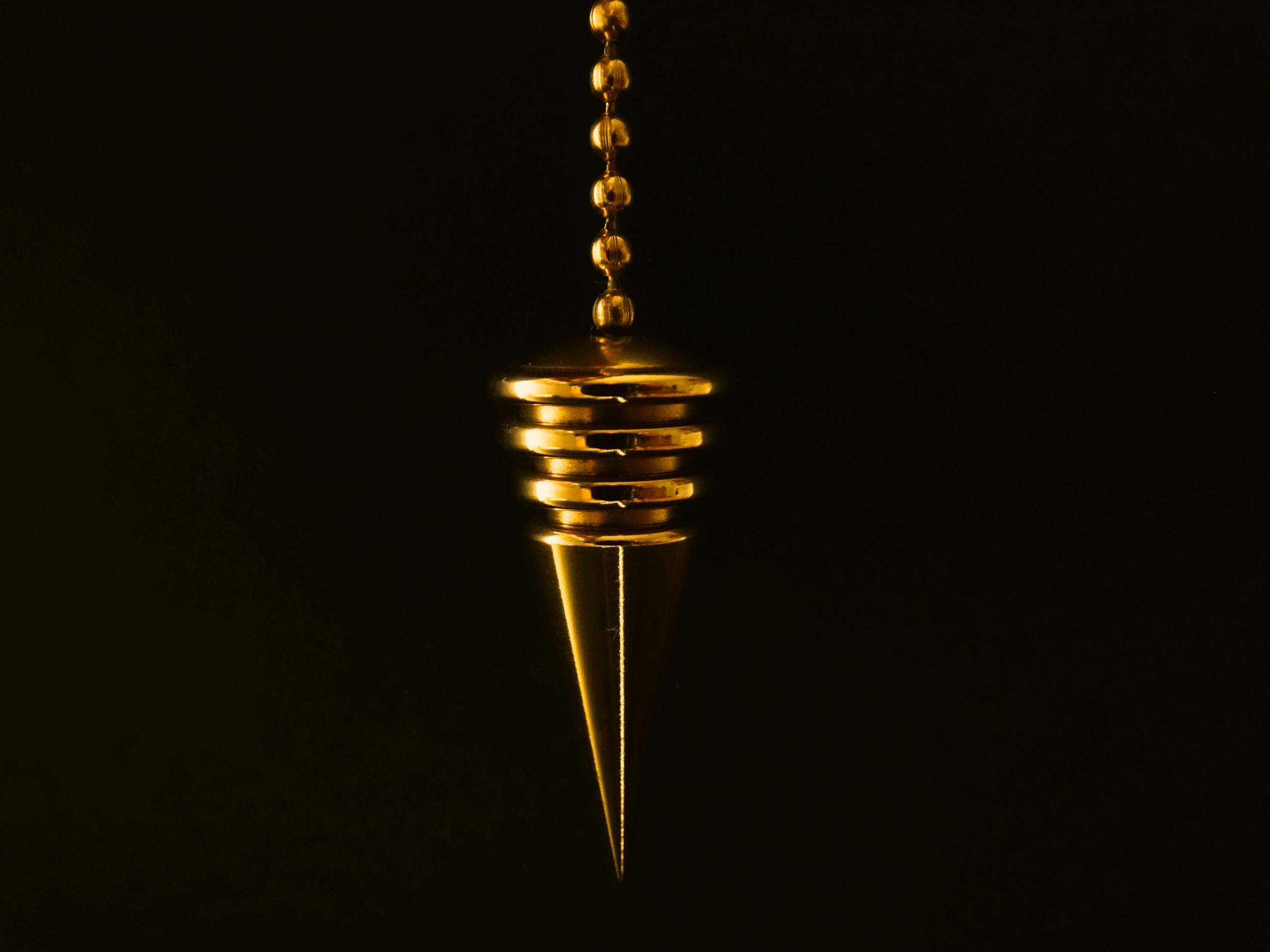 An elegant gold pendulum with chain on a mysterious black background.