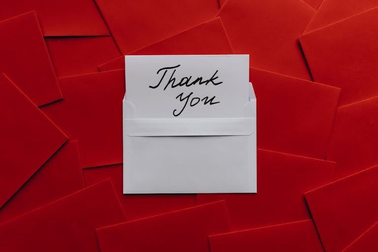 Elegant thank you card in white envelope on vibrant red envelopes flatlay. Perfect for gratitude themes.